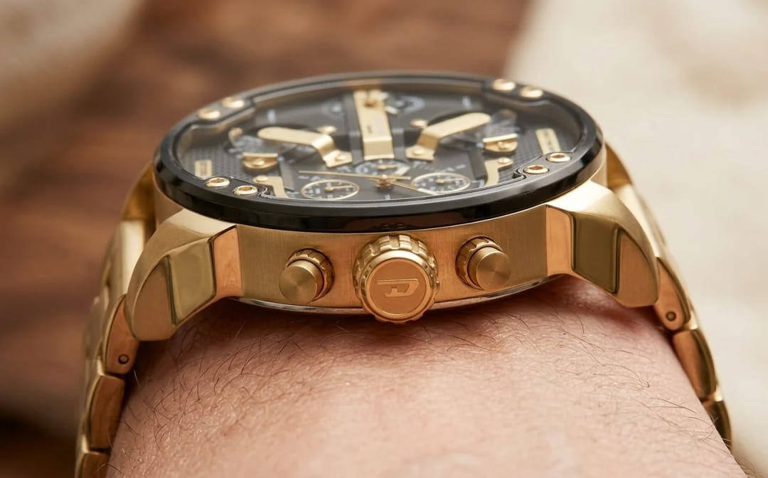 Macro side view of the Diesel DZ7333 on a man's wrist: main crown engraved with the Diesel D logo, two chronograph pushers, thick gold PVD case, gold-plated steel strap