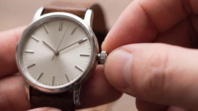 Couronne de montre en acier tirée au deuxième cran entre le pouce et l'index, pour régler l'heure