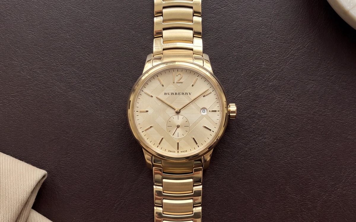 Burberry The Classic BU10006 yellow gold-tone watch with small seconds at 6, on a brown leather blotter