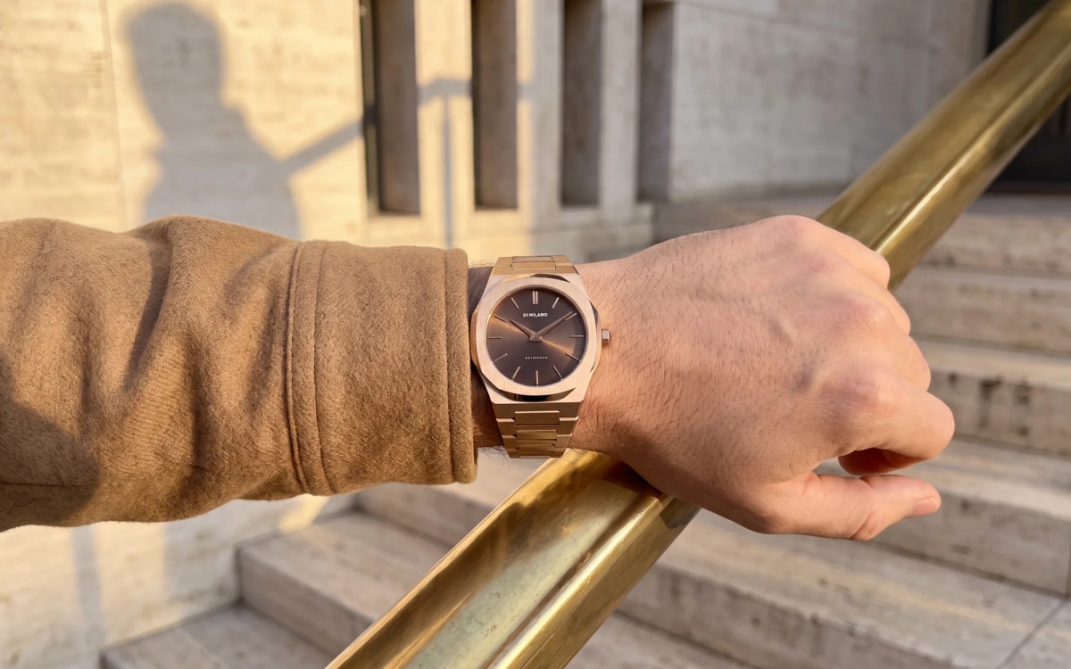 Rose gold D1 Milano Ultra Thin with a chocolate dial worn on a brass handrail