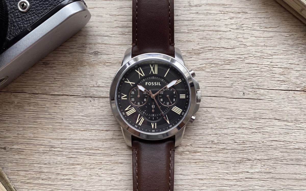 Fossil FS4813 steel chronograph with Roman numerals and brown leather strap on raw oak beside a film camera