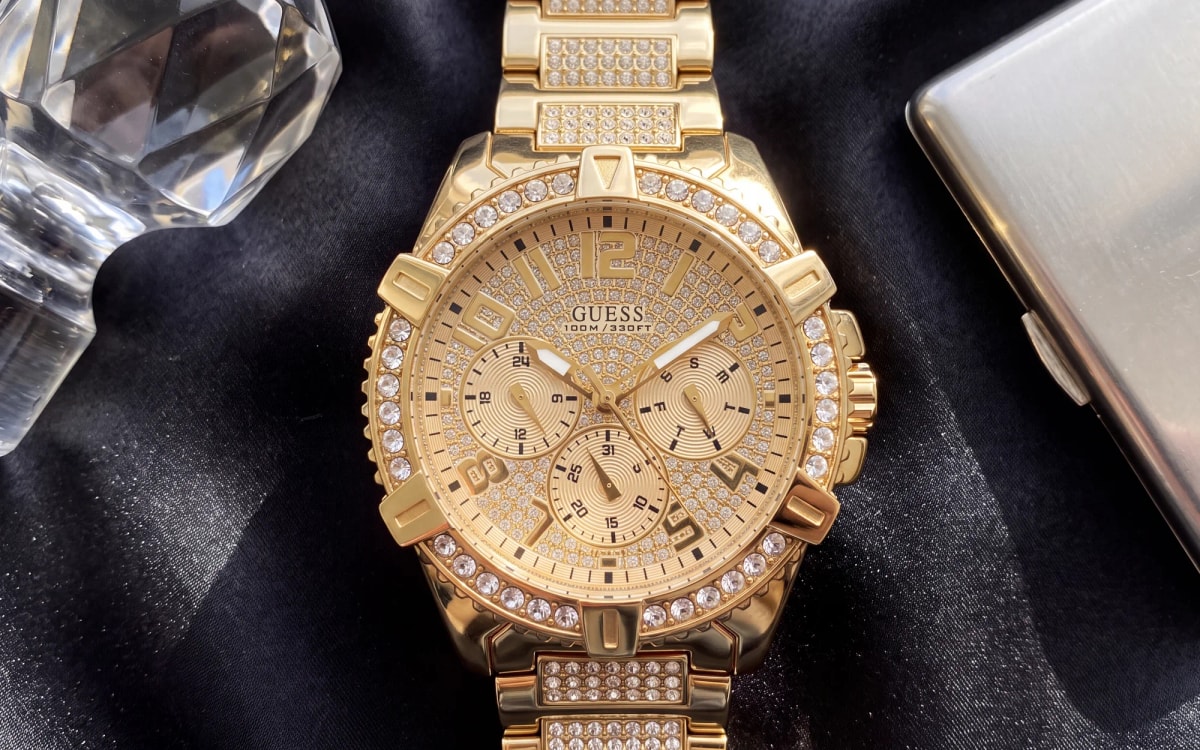 GUESS Frontier W0799G2 gold-tone men's watch fully set with crystals on black satin beside cut crystal