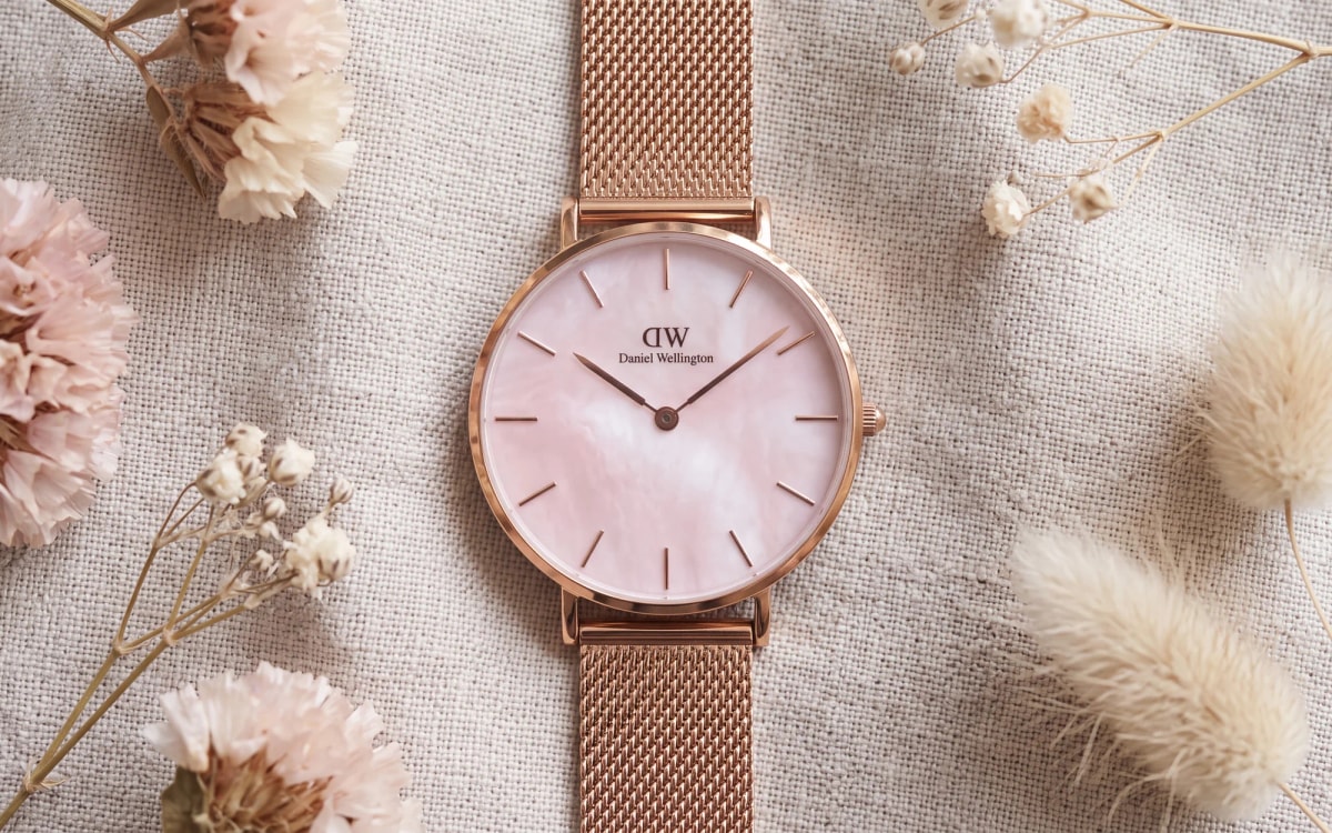 Montre Daniel Wellington Petite Melrose or rose, cadran nacre rose, posée sur du lin clair parmi des fleurs séchées