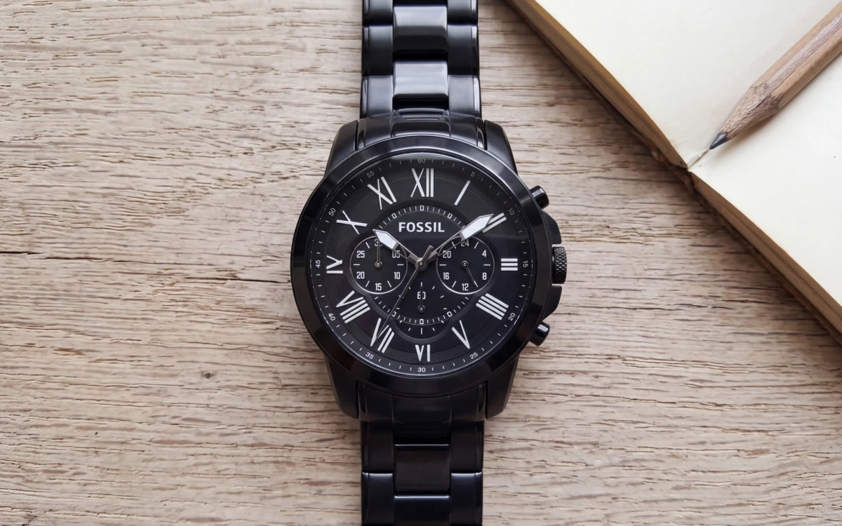 Montre homme Fossil Grant FS4832 noire, chronographe à chiffres romains, posée sur chêne près d'un carnet ouvert