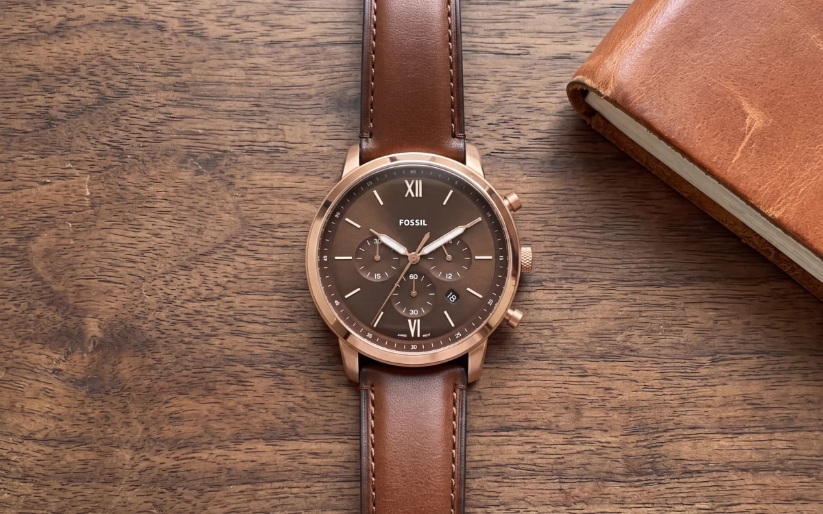 Montre homme Fossil Neutra FS6026 or rose, cadran chocolat et cuir marron, posée sur noyer près d'un carnet