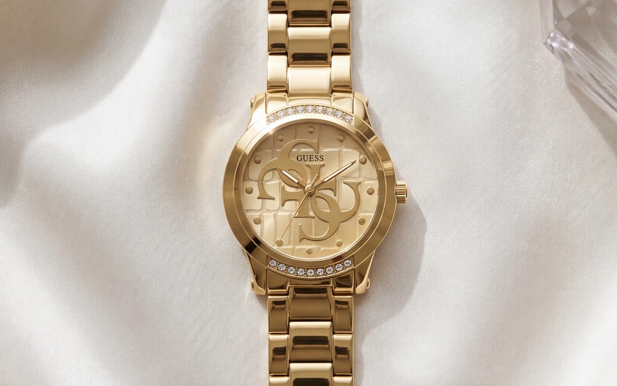 Montre femme GUESS Annette GW0861L2 dorée au monogramme 4G, sur satin ivoire près d'un flacon en cristal