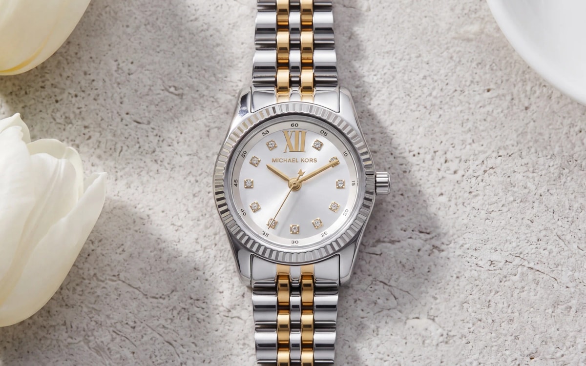 Montre femme Michael Kors Petite Lexington MK4740 bicolore, cadran argenté, posée sur pierre près de tulipes