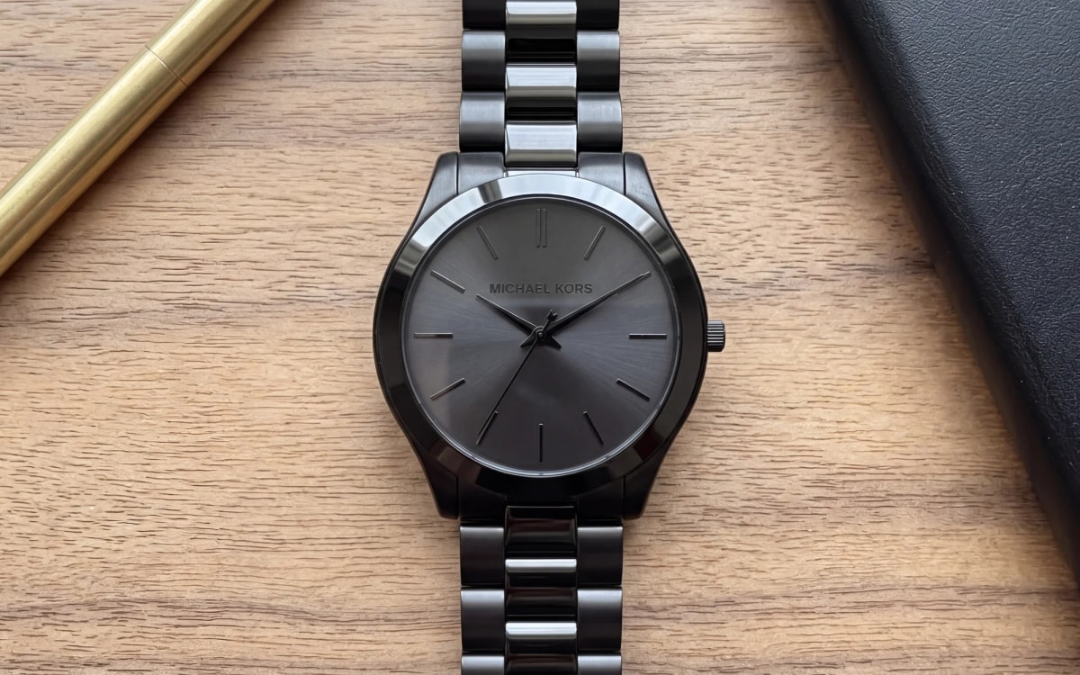 Montre homme Michael Kors Slim Runway MK8507 entièrement noire, posée sur un bureau en noyer clair