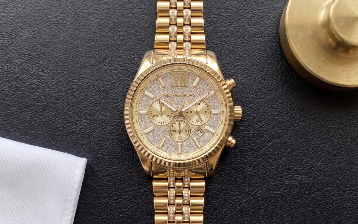 Montre homme Michael Kors Lexington MK8579 dorée, cadran pavé de cristaux, posée sur un sous-main en cuir noir
